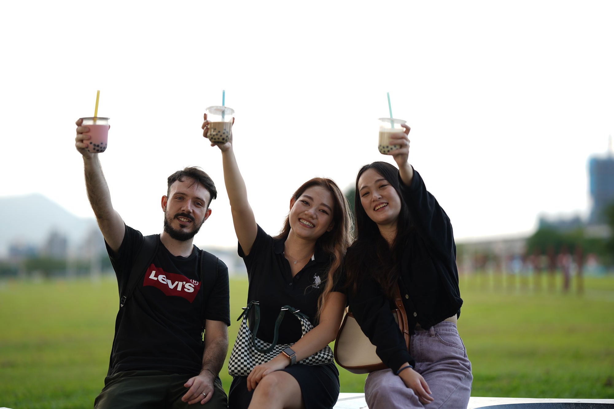 2 women and 1 man holding bubble tea with their hands raised and smiling