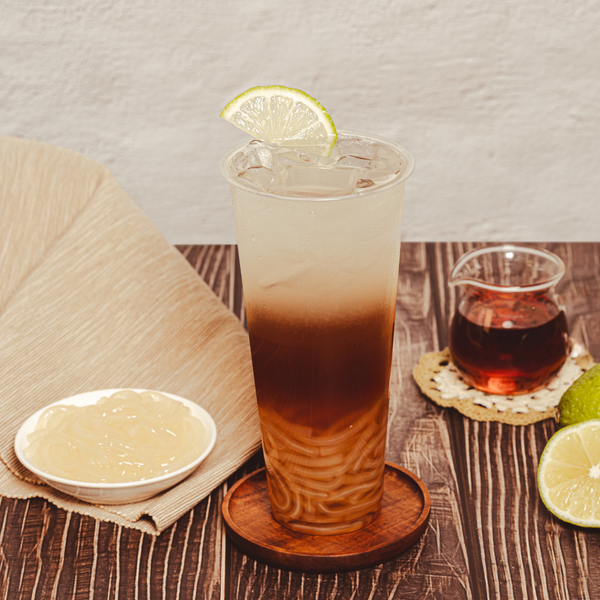 Glass of layered iced tea with QQ Tapioca Noodles and a lime wedge on a wooden table. view 4
